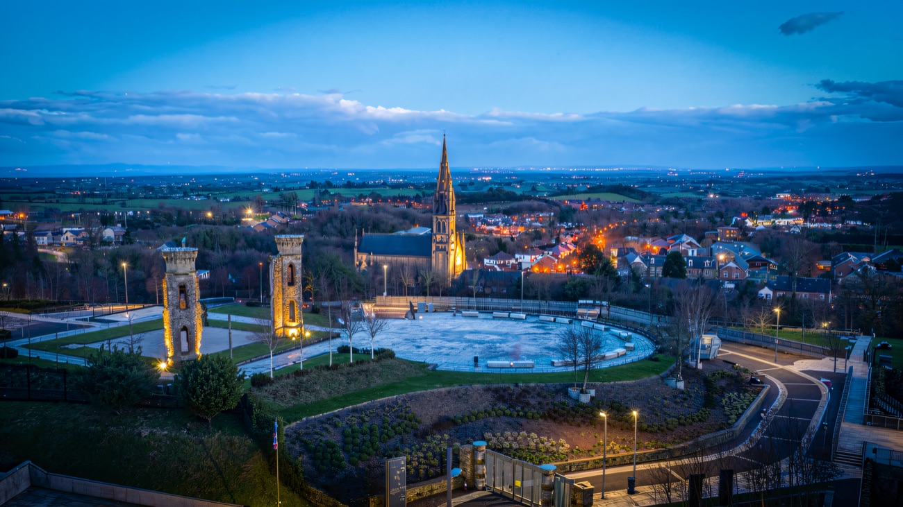 Blue-hour view over the floodlit towers, the town and the vast plain of Tyrone stretching to the horizon.