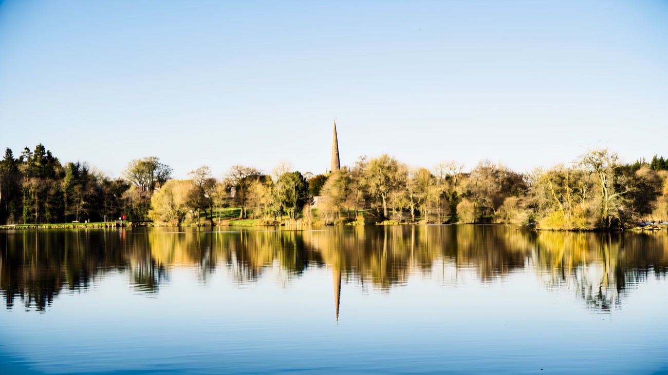 Still water at Hillsborough Lake with the parish church spire and bare winter trees mirrored on the surface