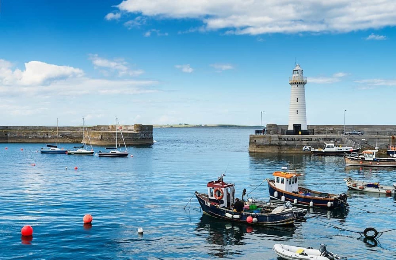 Donaghadee harbour and the white lighthouse under a bright blue sky with boats on calm water