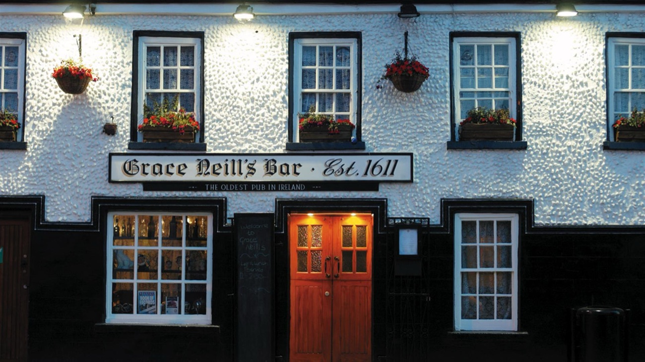 Grace Neill's Bar in Donaghadee, its whitewashed frontage lit at dusk, with the Est.1611 sign above the door