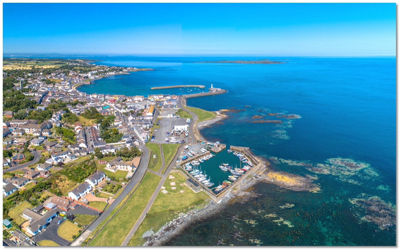 Aerial view of Donaghadee town, its harbour, lighthouse and marina wrapping around the blue bay