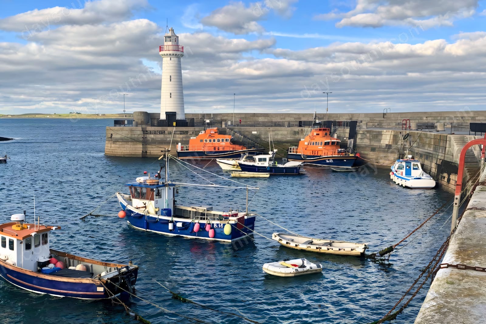 Donaghadee harbour with its white lighthouse, lifeboats and colourful fishing boats moored inside the stone pier
