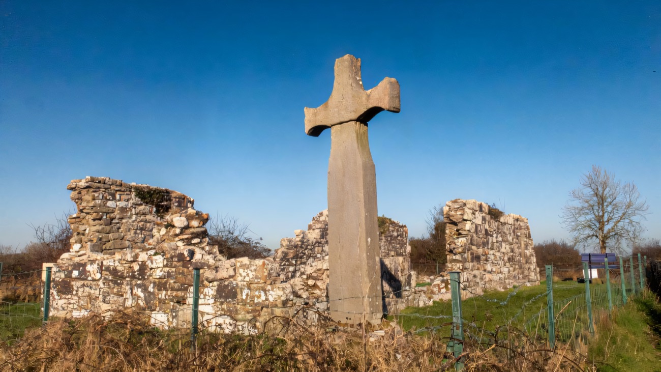 The tall, unadorned high cross standing against a clear sky.