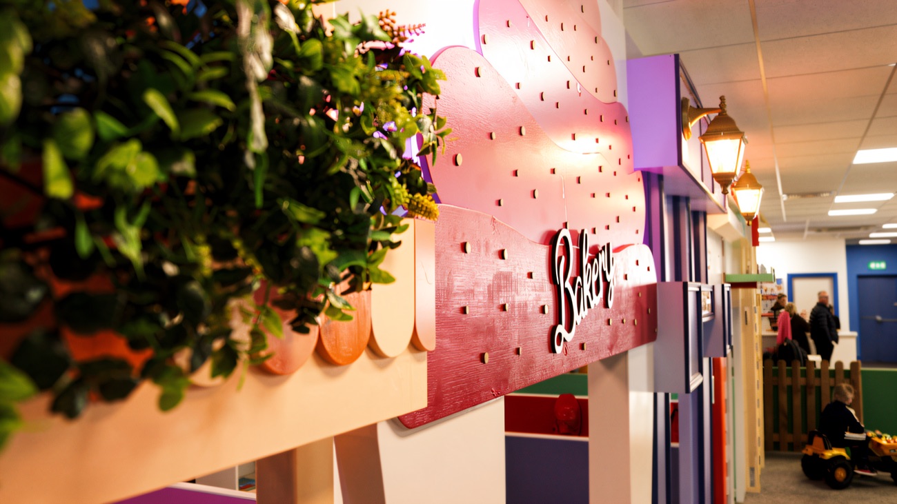 The pastel pretend-play street with a bakery shopfront, trailing greenery and vintage-style lamps