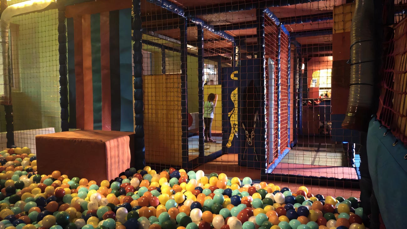 A colourful ball pool with hundreds of coloured balls beneath the netted soft play maze