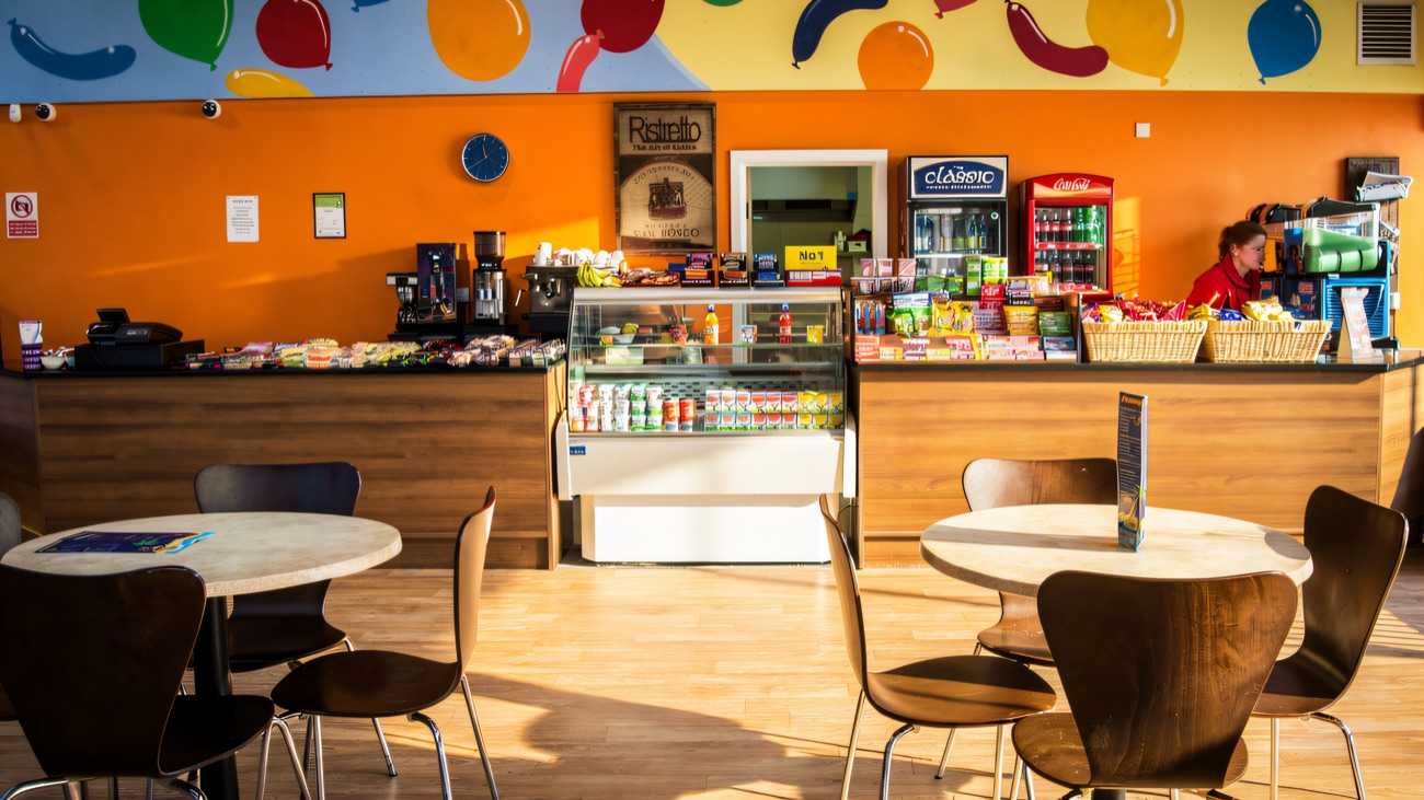The cafe counter under a painted balloon mural, with coffee machine, snacks and round tables