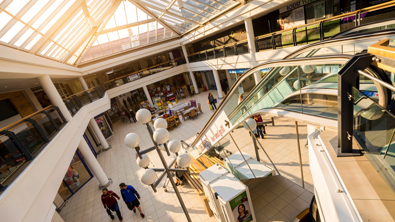 The bright atrium of the Kennedy Centre under its pitched glass roof, with the white globe lamp-post and shopfronts below