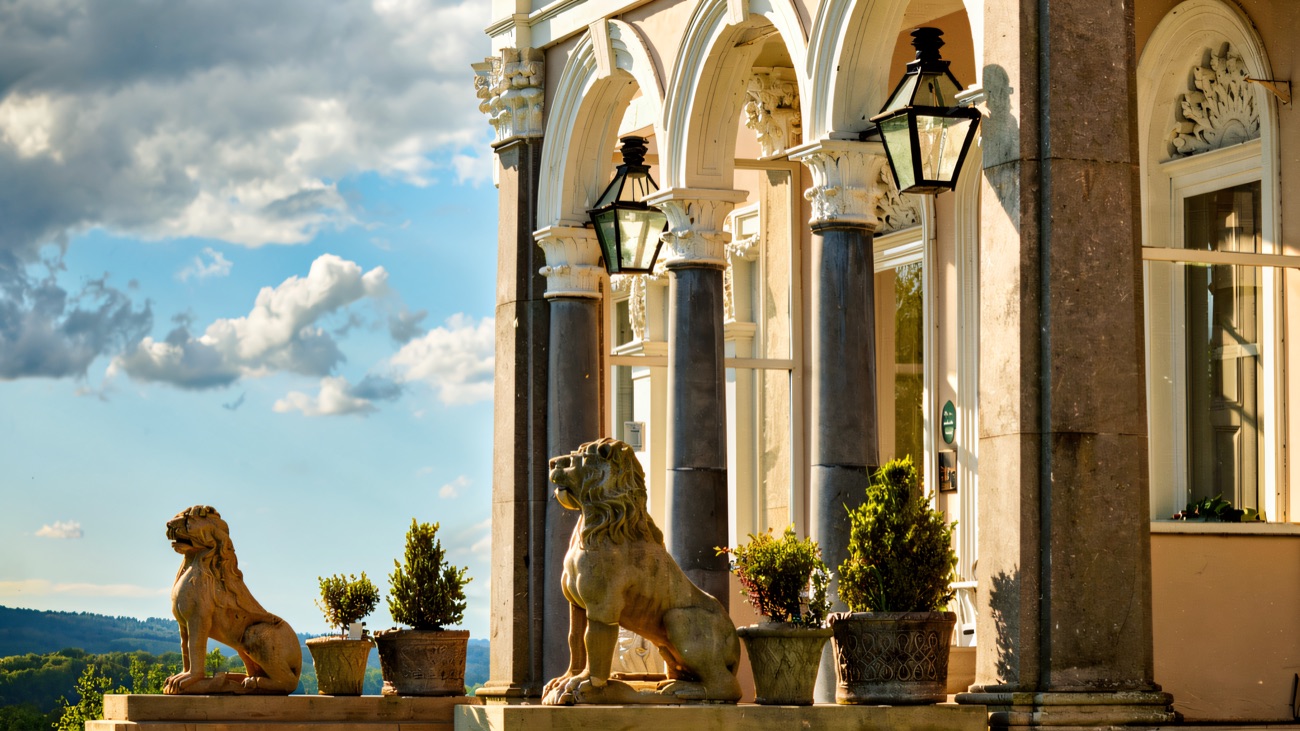 The arched stone colonnade at the entrance to the manor, flanked by carved stone lions and potted bay trees