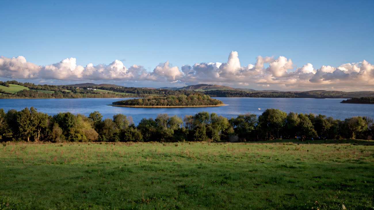 A calm stretch of Lower Lough Erne with a wooded island and low green hills beyond
