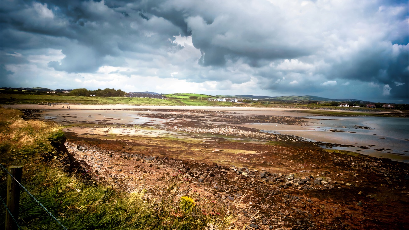 The rocky shore at low tide, storm clouds gathering over the fields