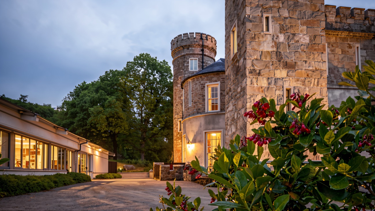 The Gothic castle's battlemented stone tower, the low spa building beside it and flowering shrubs in front.