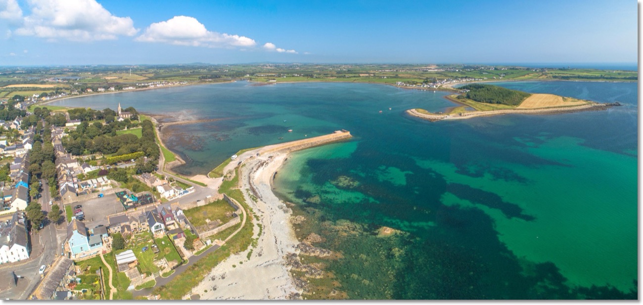 Aerial view over the village of Killough, its church spire and tree-lined streets, with the beach and Coney Island Bay stretching out beyond