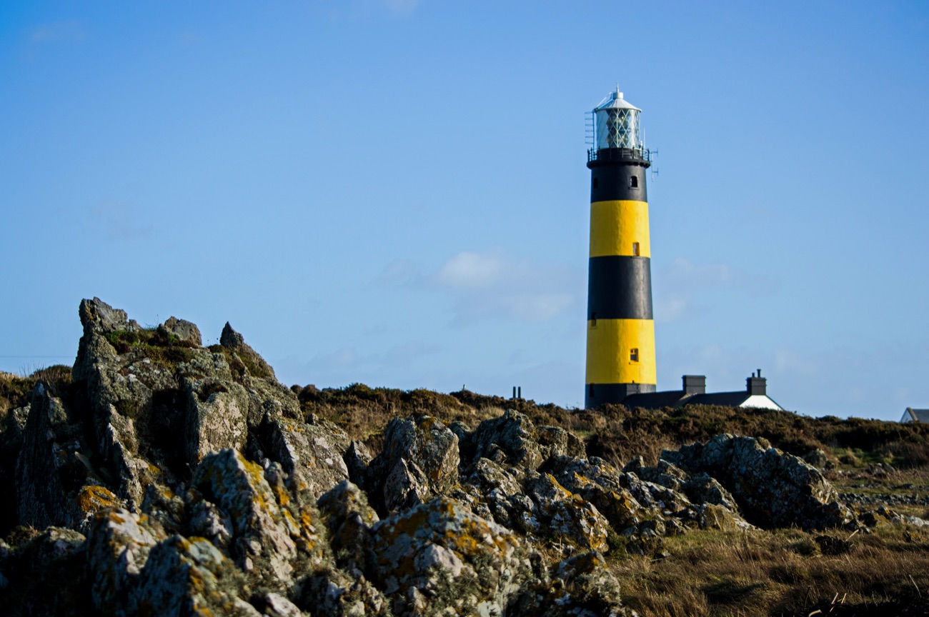 The black-and-yellow banded tower of St John's Point lighthouse standing above rocky ground near Killough under a blue sky