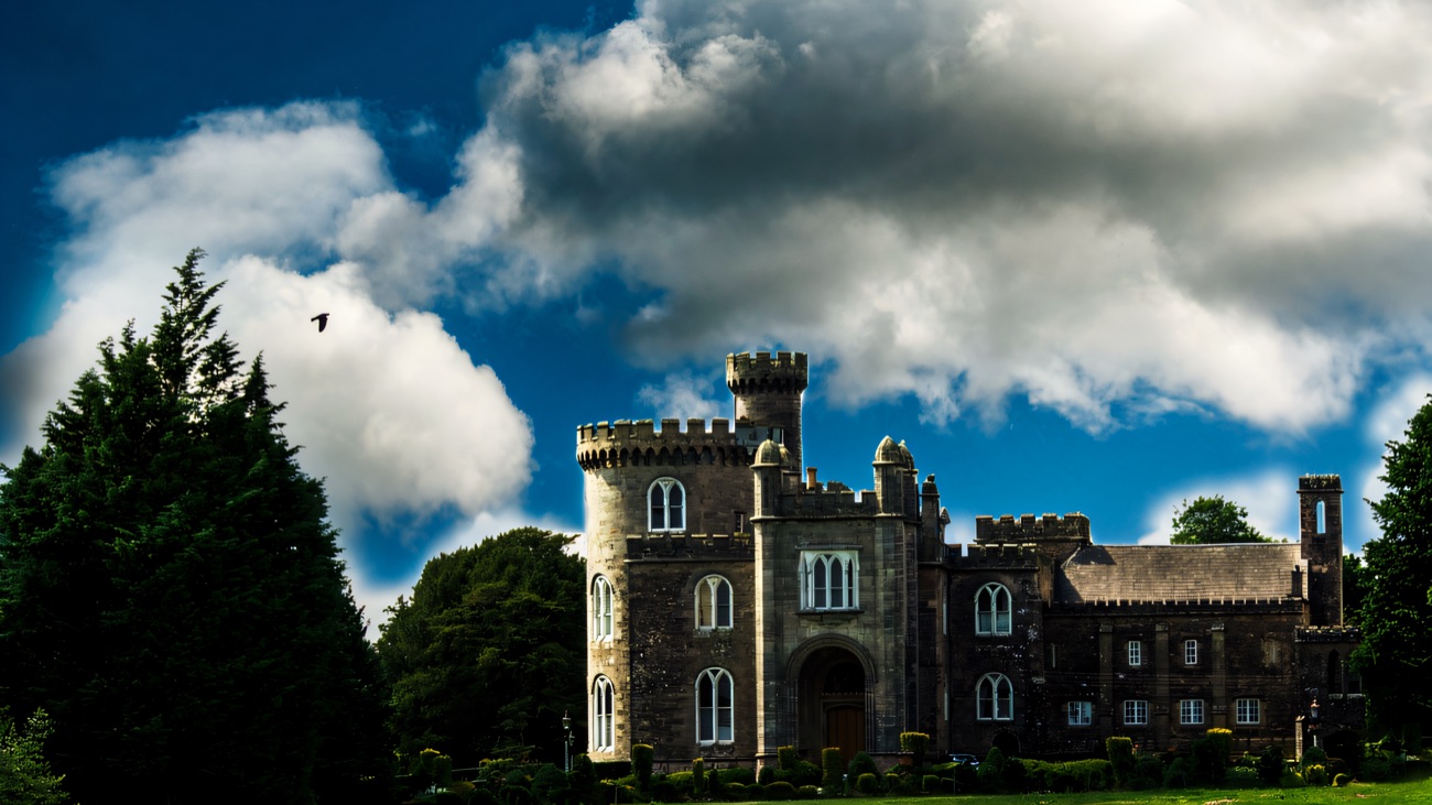 Killymoon Castle seen from the front under a big sky, its round tower and battlements rising above the parkland trees