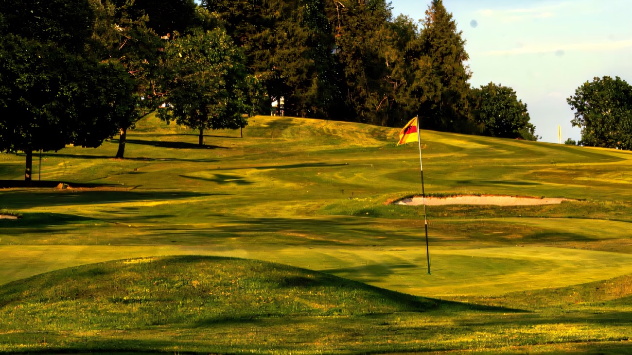 A green and flag on the parkland golf course at Killymoon, with mown fairways, bunkers and mature trees