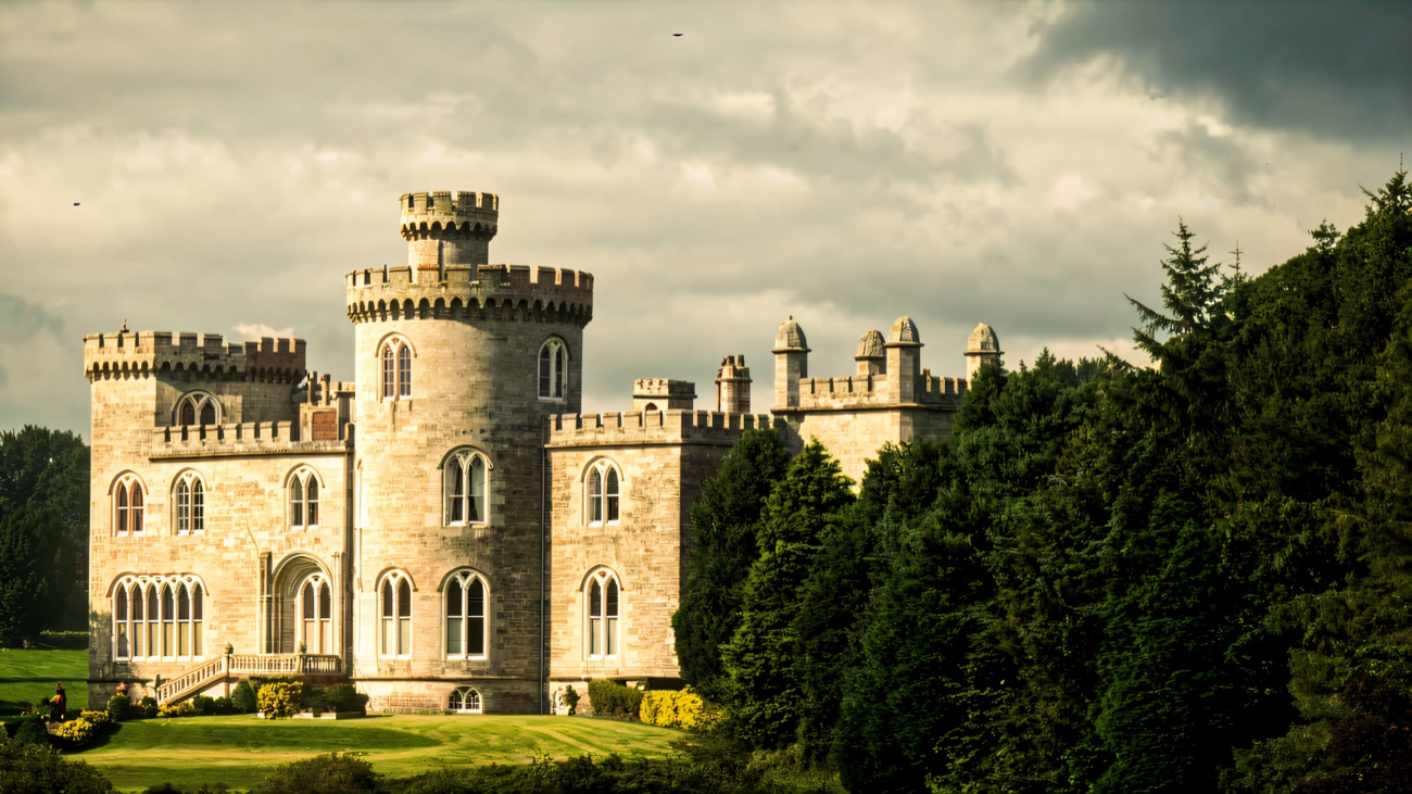 Close view of Killymoon Castle's battlemented round tower and turrets in pale stone against a cloudy sky