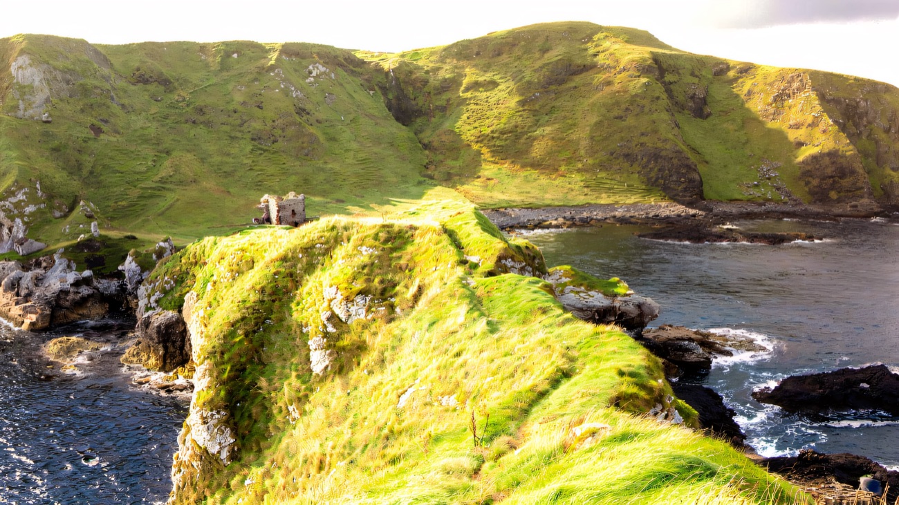 The green headland reaching out into the sea, the ruins at its far tip.
