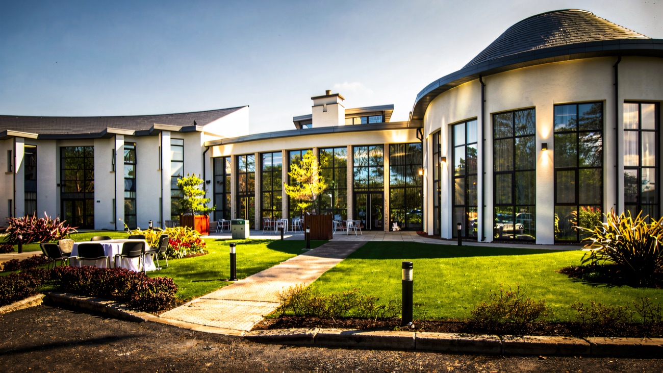 The white, curved façade of La Mon Hotel and Country Club under a bright sky, with lawns out front.