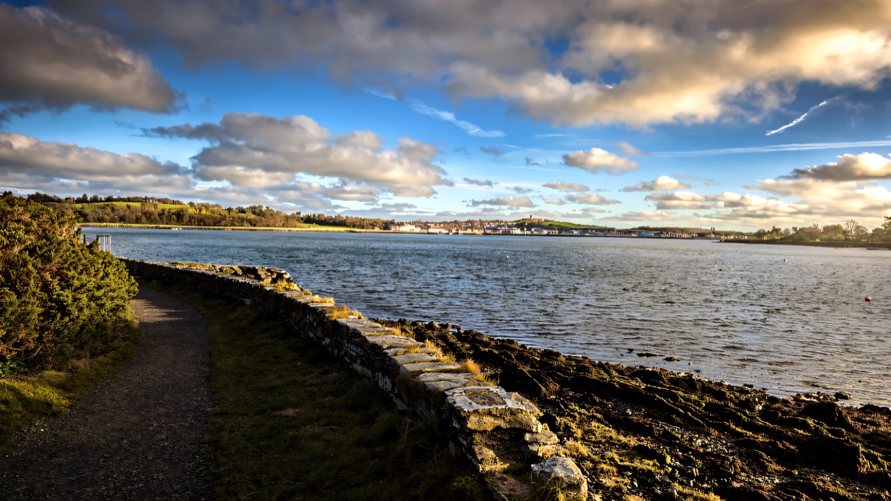 A stone-walled coastal path along the water, a town across the bay
