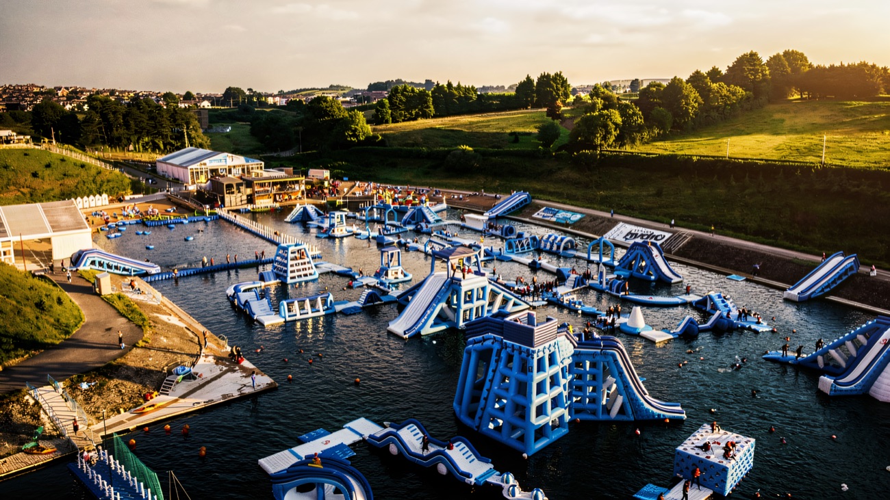 A sunny aerial view of the Let's Go Hydro inflatable aqua park spread across the lake with green hills behind