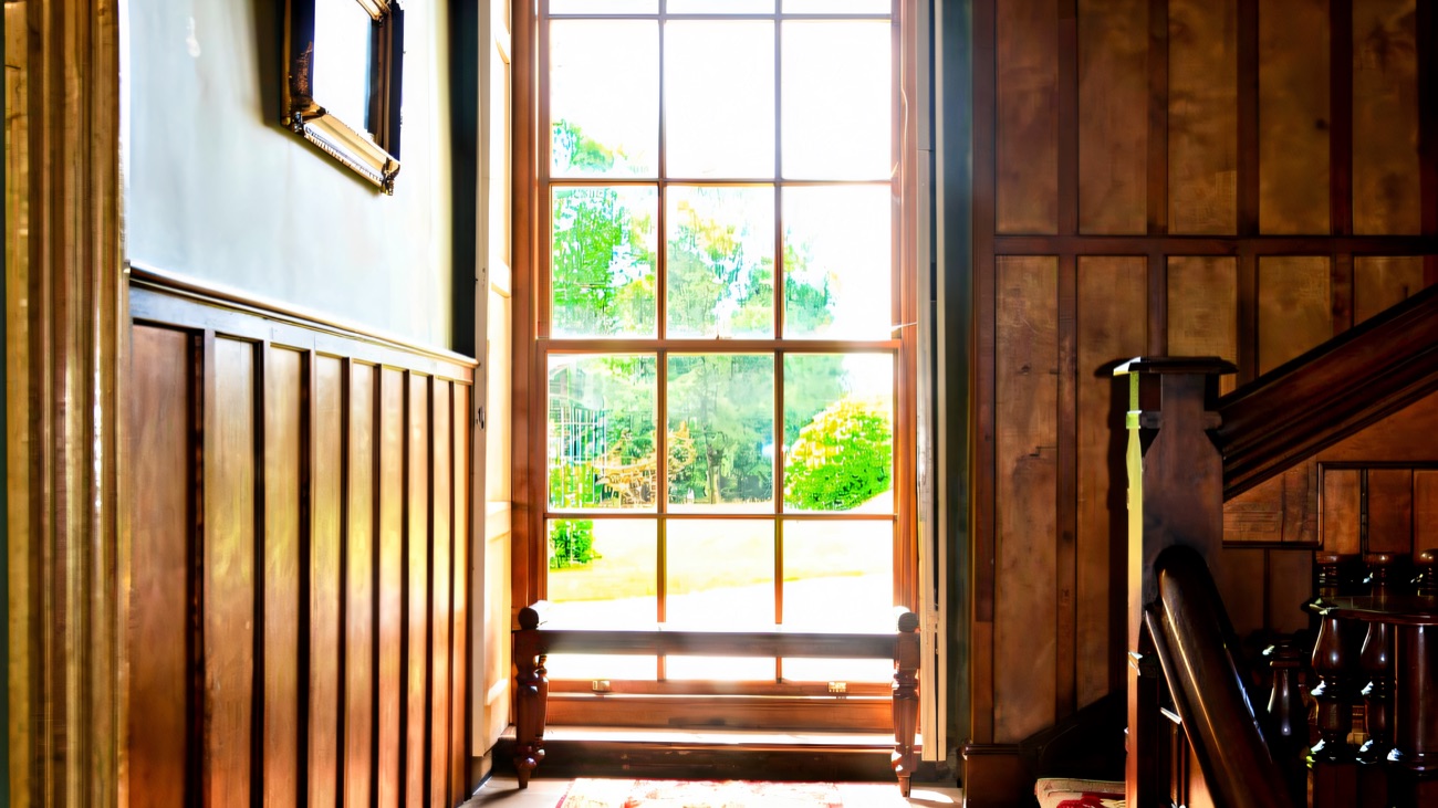 A dark oak-panelled staircase landing inside Lissan House, with a patterned red runner and a tall window looking out to the grounds