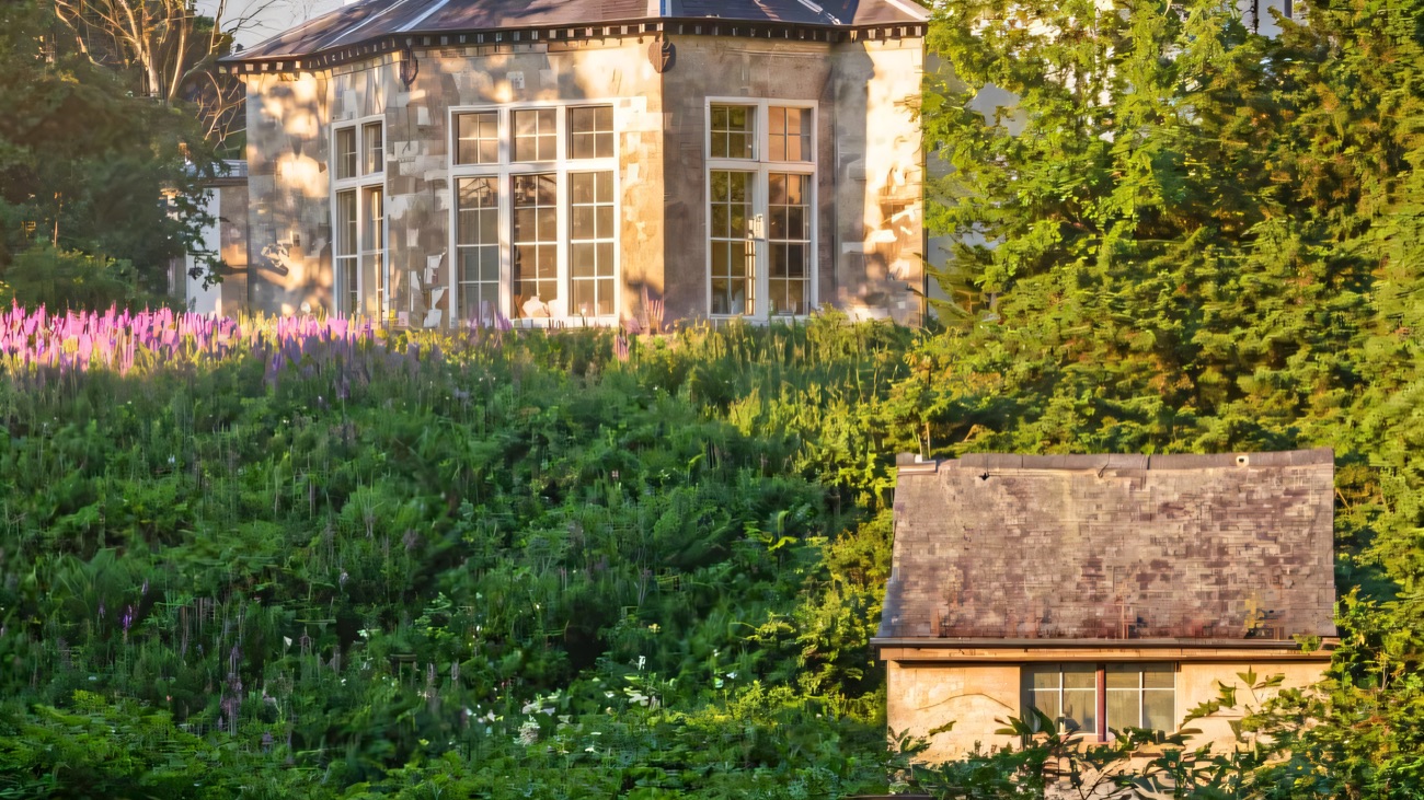 The stone bow wing of Lissan House rising above a lush garden of tall flower spikes and giant leaves, with a small stone garden building