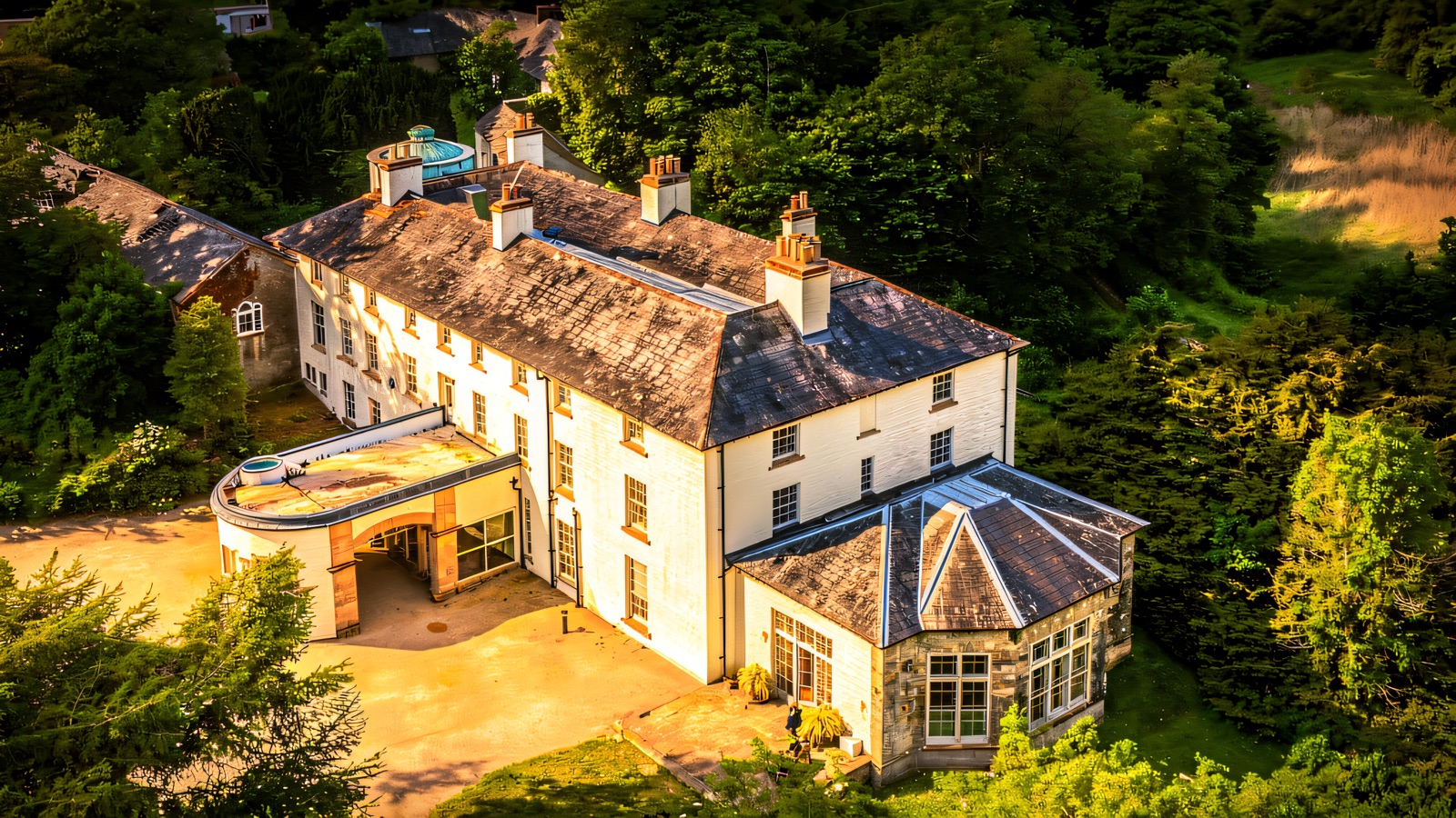 An aerial view of the white rambling manor of Lissan House set among green woodland, with its stone bow-window wing