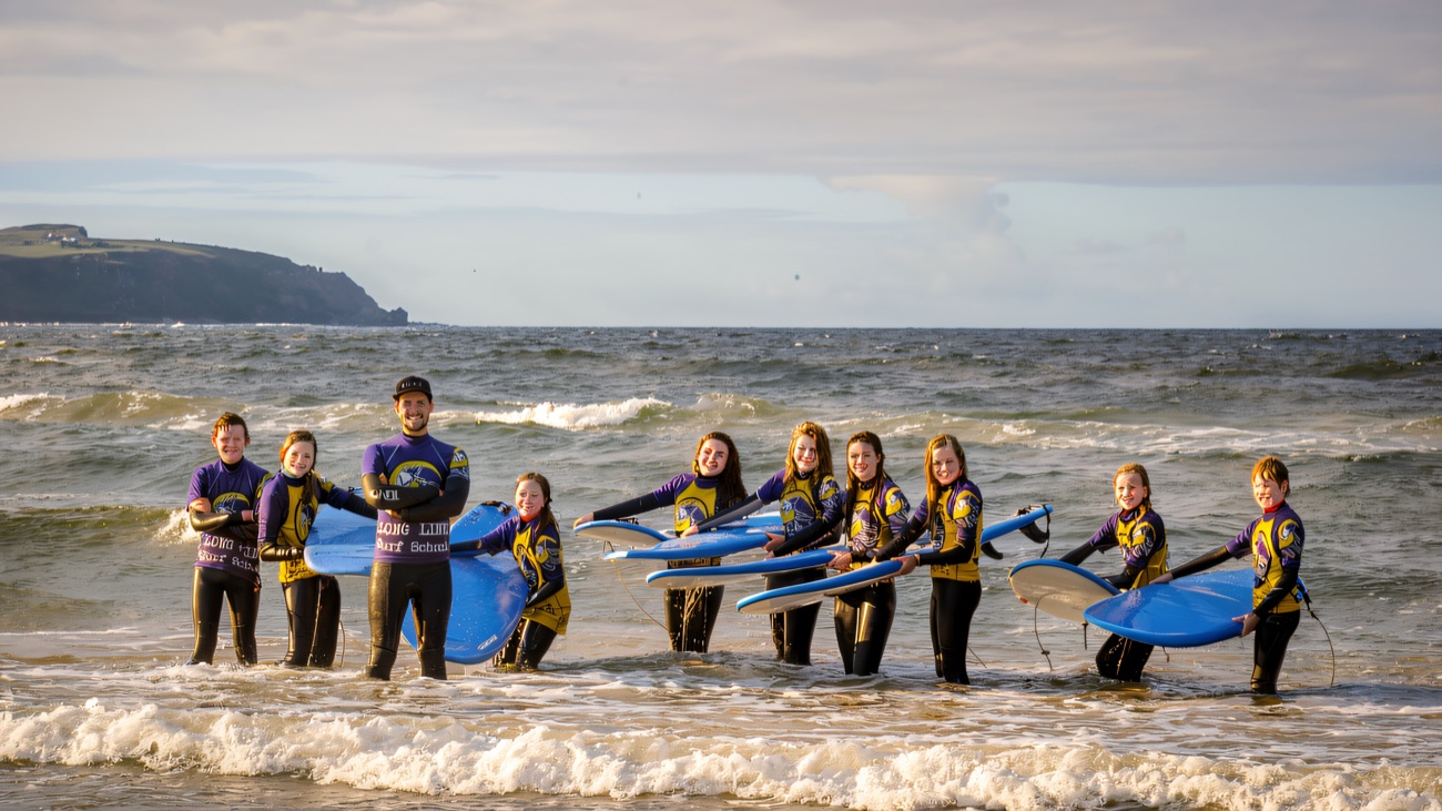The Long Line crew grinning in the shallows, boards ready to go