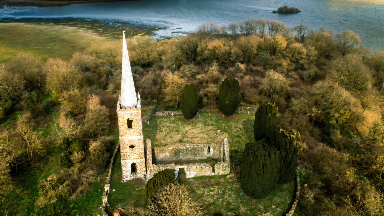 The ruined church and spire from above in winter light, the flooded lough margins all around.