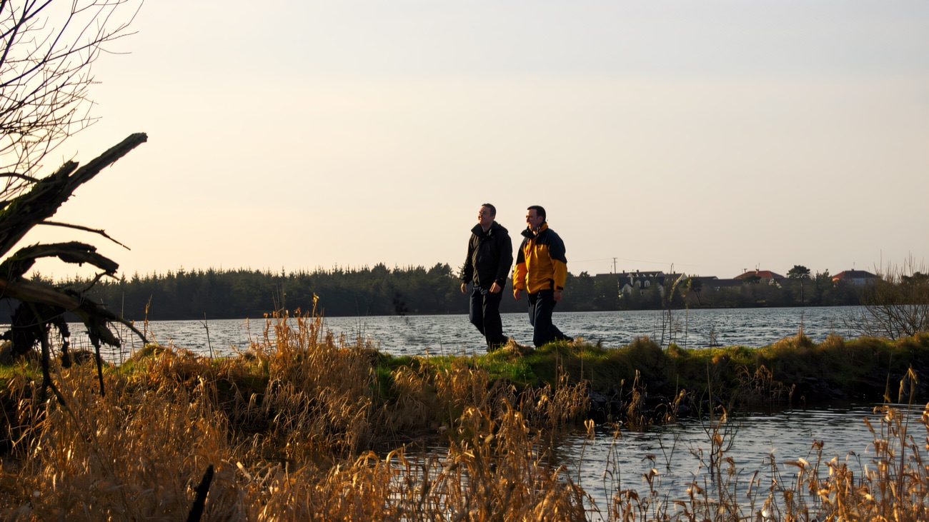 Walkers follow the shoreline path, the quiet lough stretching out beside them