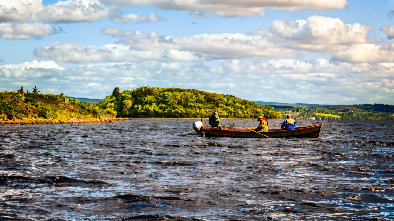 Three anglers drifting past a wooded island on the lough