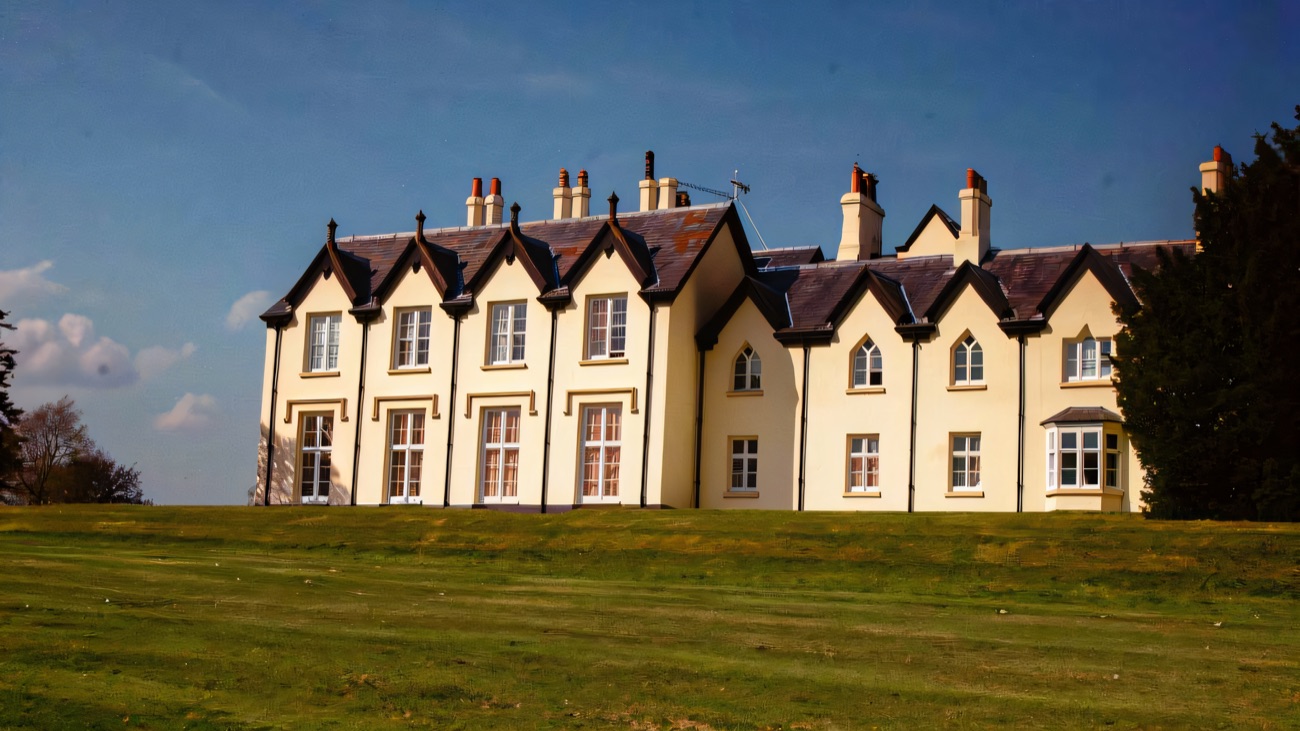 The full front elevation of Loughgall Manor across a broad lawn in spring sunshine
