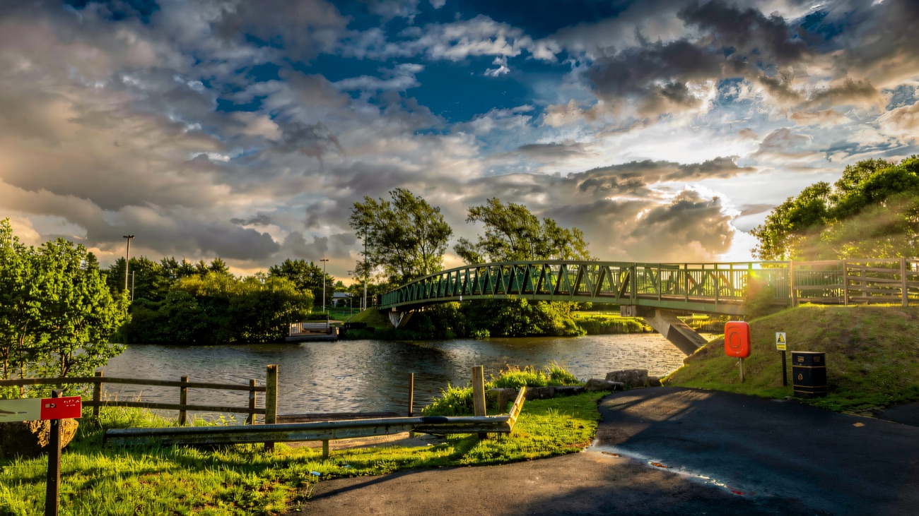 A green footbridge carries the trail over the water under a big sky