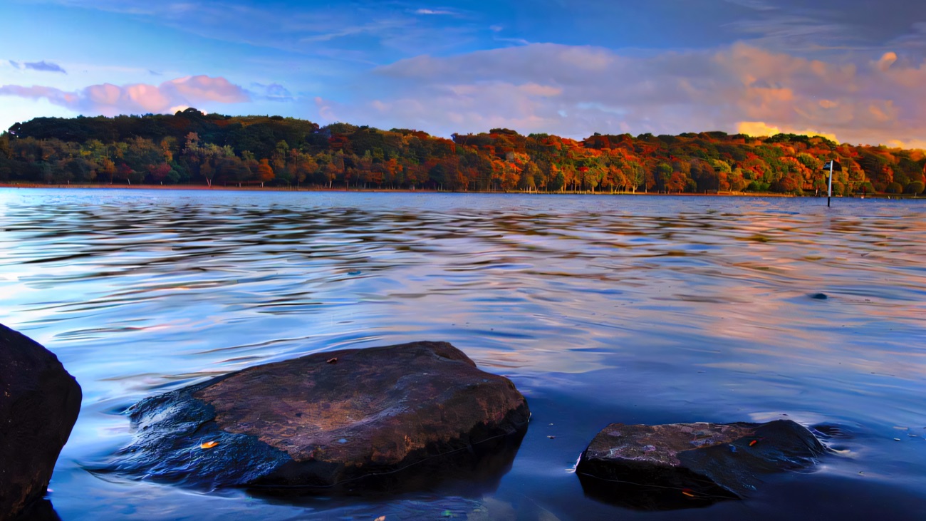 Autumn colour reflects on still water among the shoreline rocks.