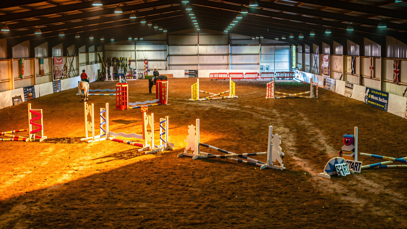 The big indoor arena with a colourful course of jumps set out and riders working at the far end