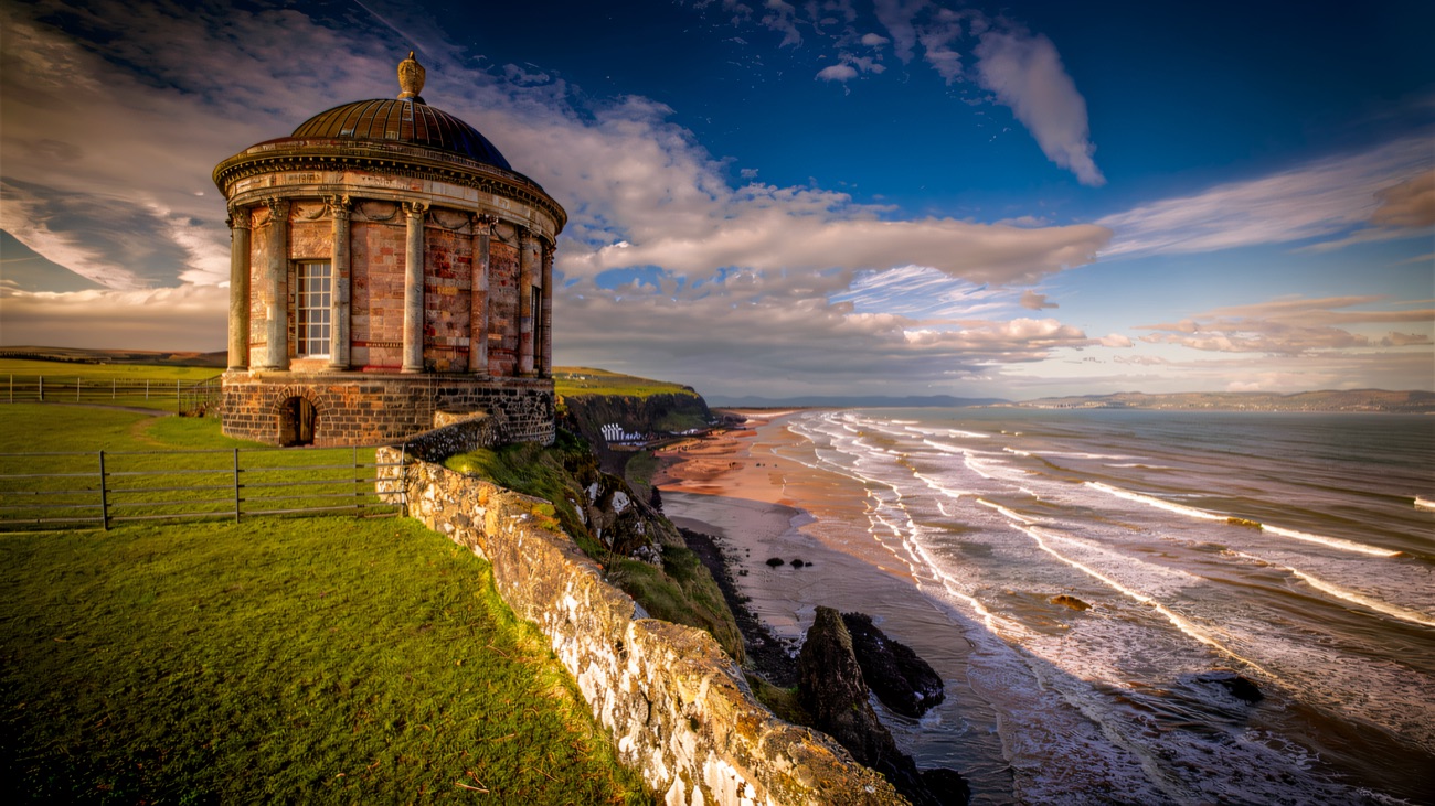 A domed stone temple perched on the clifftop, with white surf rolling onto the long beach far below