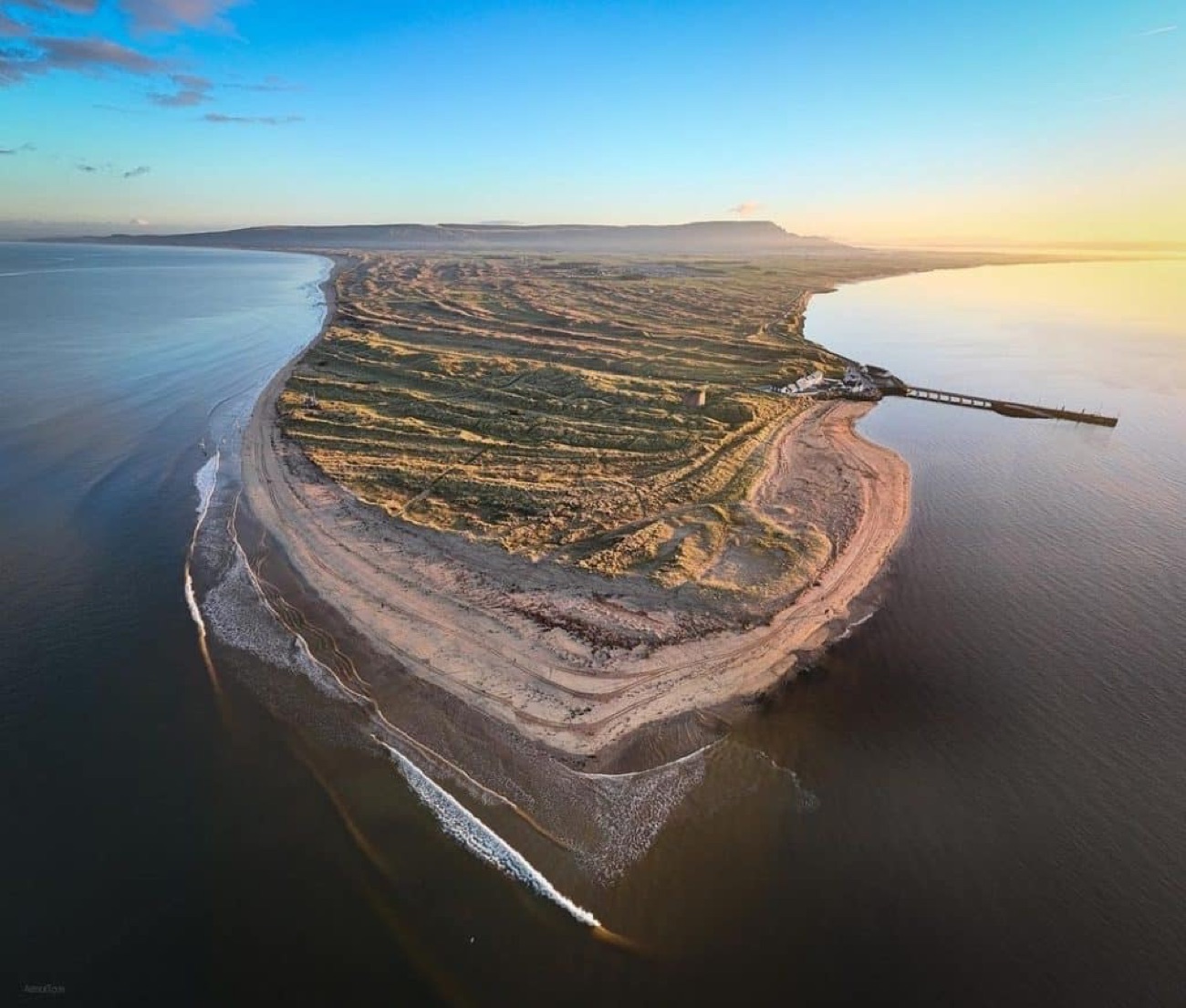 Aerial view of the vast Magilligan dune system reaching out into the sea at the mouth of Lough Foyle in golden evening light