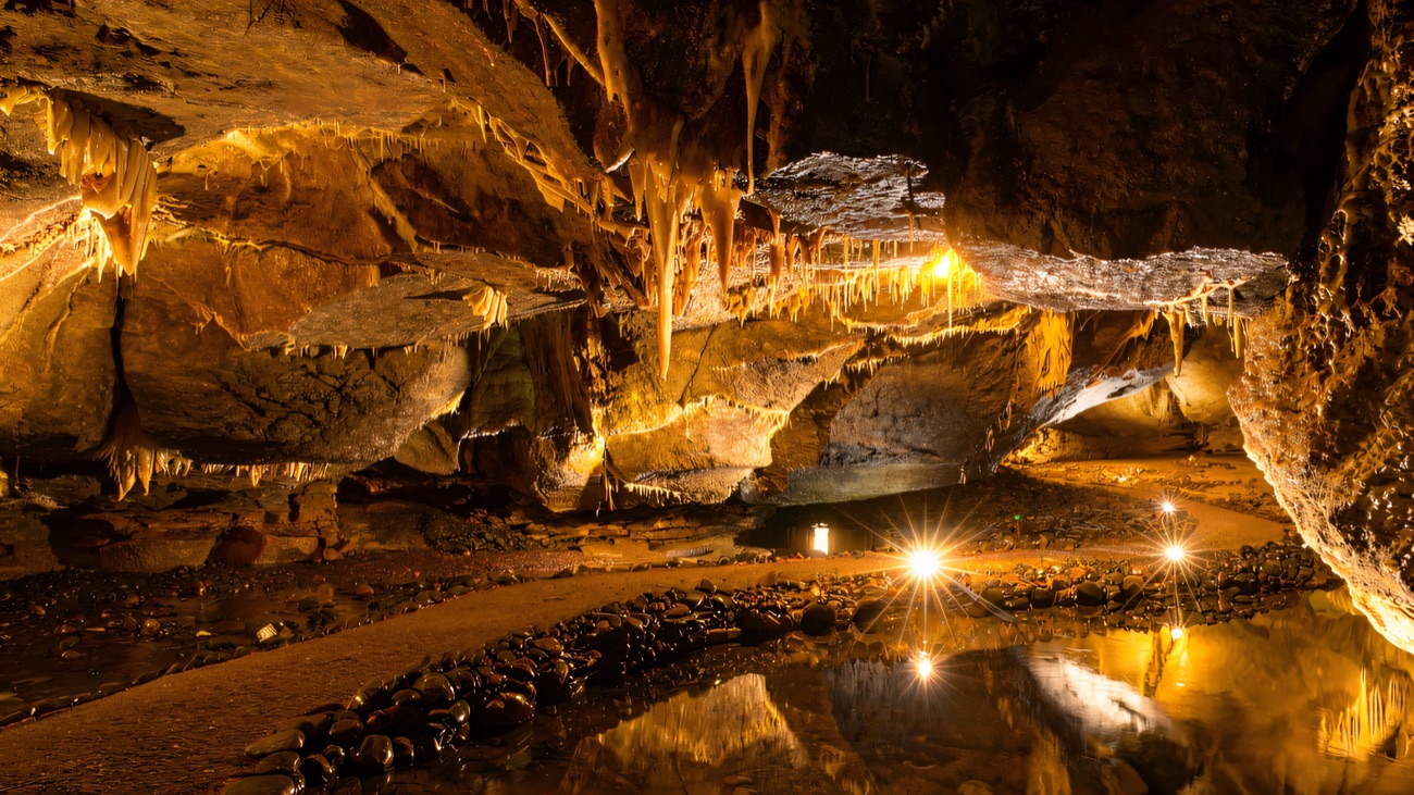 A floodlit chamber of hanging stalactites doubled in a still black pool