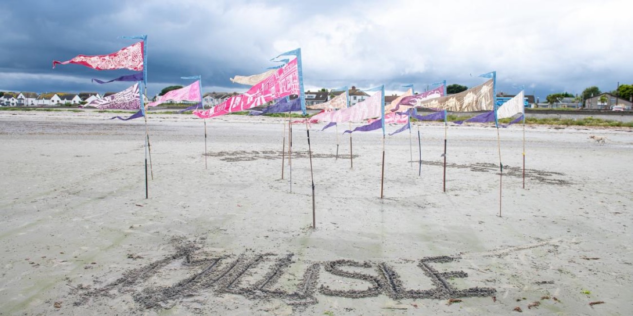 Colourful bunting flags fluttering on the wide open sand at Millisle beach with MILLISLE written in the sand and the village behind