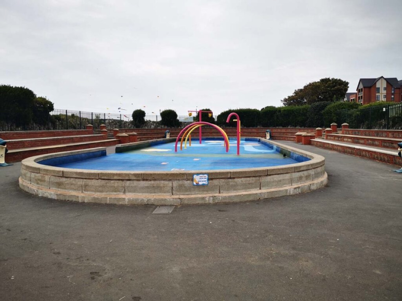 The children's splash and paddling pool at Millisle with bright pink water arches, ringed by a low stone wall and promenade