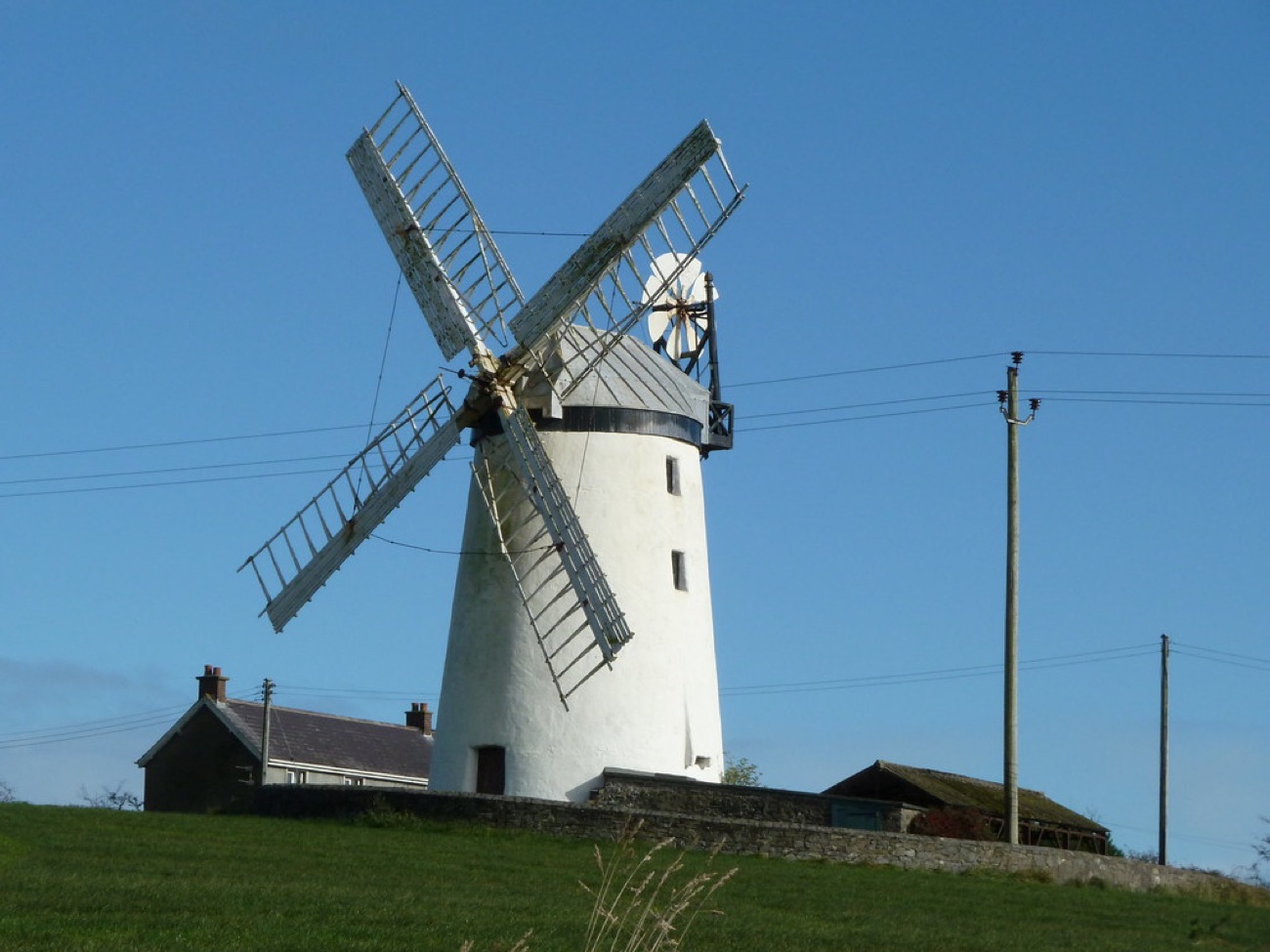The whitewashed Ballycopeland Windmill with its sails and fantail against a clear blue sky, just up the road from Millisle beach