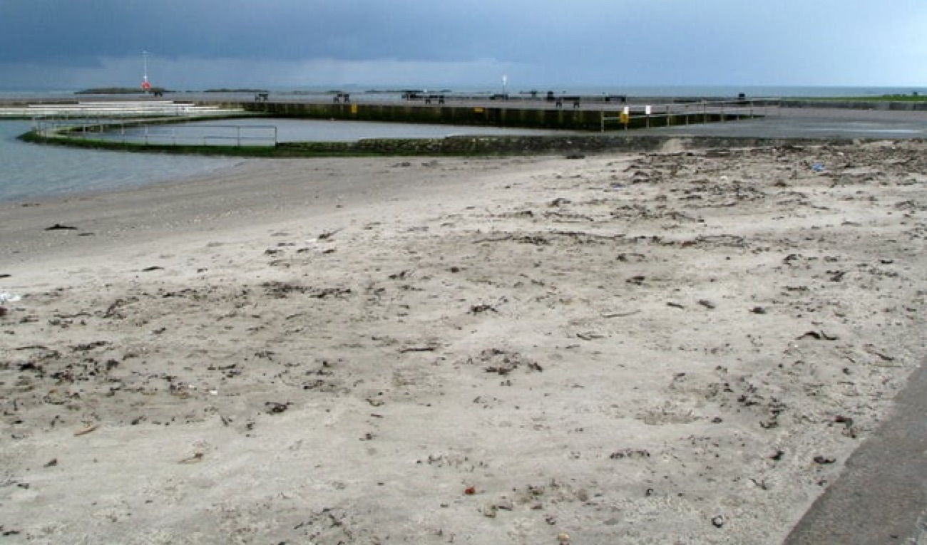 The seawater lagoon wall and jetty at Millisle where the enclosed pool meets the open sea, with wide sand in the foreground