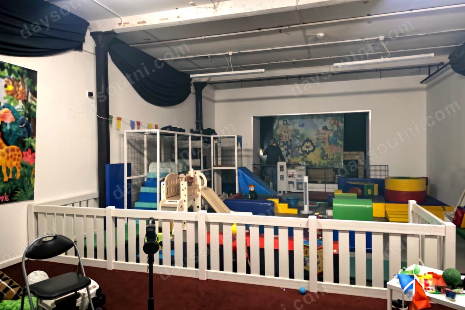 The indoor soft play area at Monkeez@TheMill in Castlewellan, with a white picket fence, a small frame, a jungle mural and soft play shapes