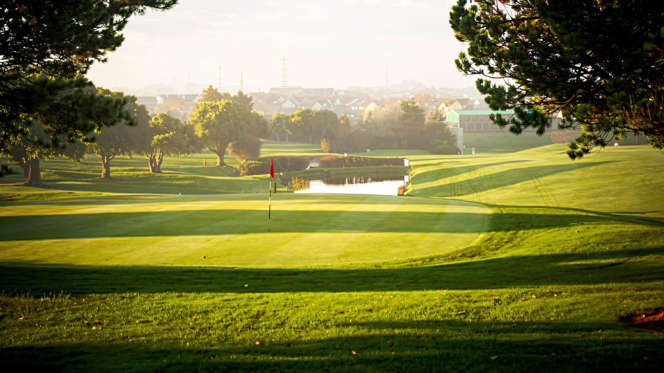 A flagged green beside a pond with the Belfast skyline in the distance