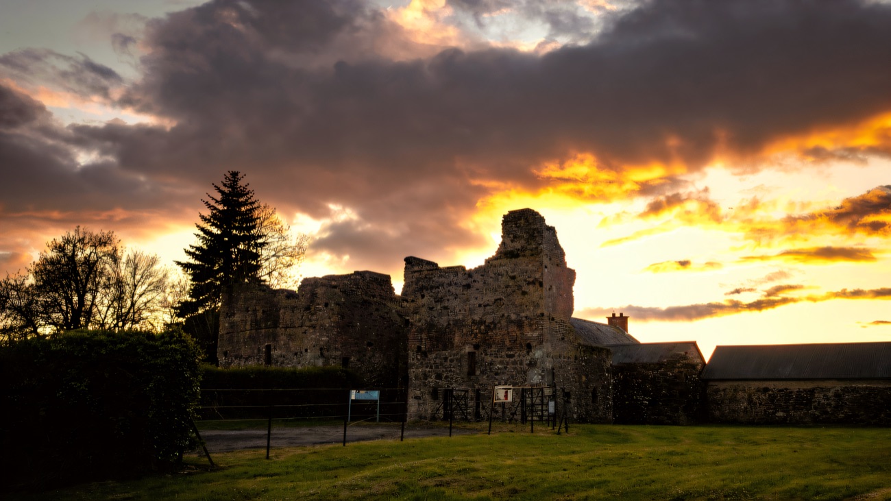 The ruined fort silhouetted against a fiery sunset, seen from across the fields.