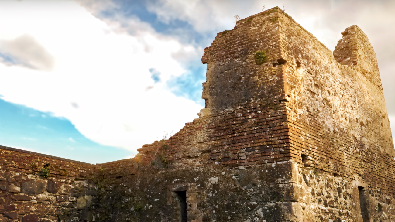A surviving corner tower, its Tudor brickwork bright against a blue and cloudy sky.