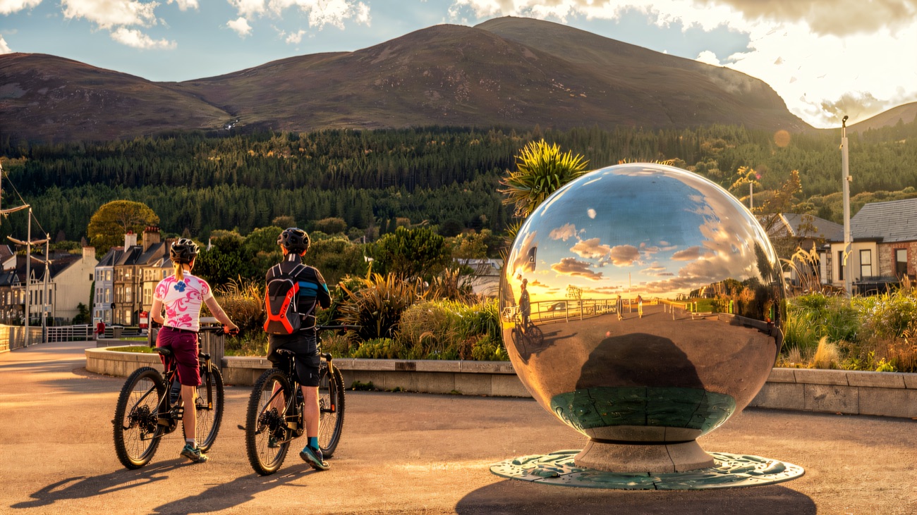 Cyclists pause on the Newcastle promenade with the mountains behind
