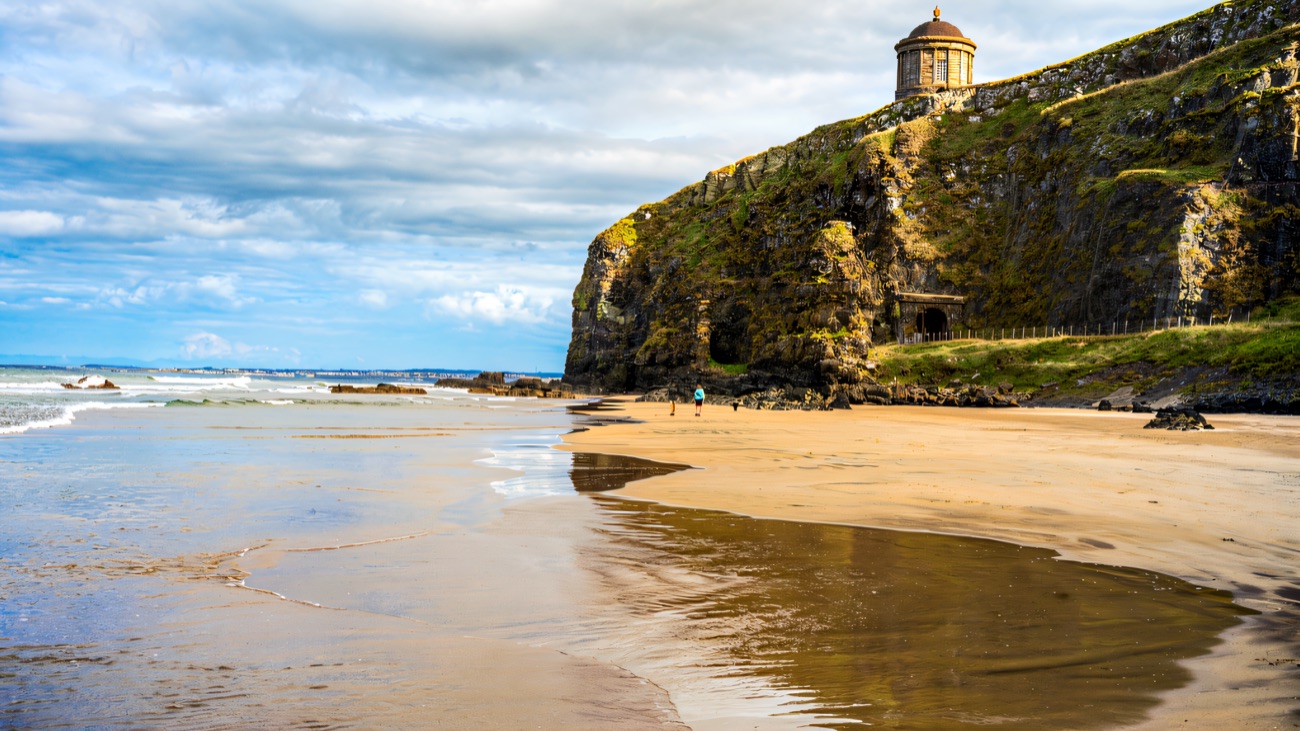 Mussenden Temple high on the cliff above the wide sweep of Downhill Strand and the cave in the headland