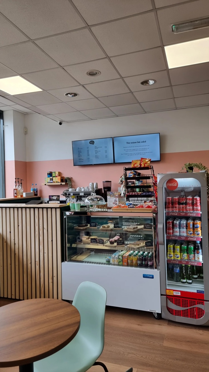 The café counter and seating at Nature and Nurture, with a chilled drinks fridge, treats and a wood-panelled counter