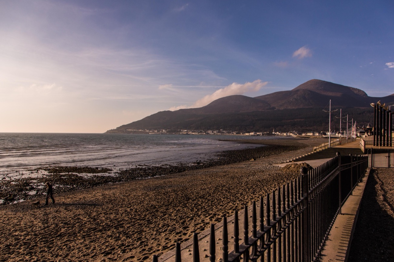 The beach and promenade railings at Newcastle in golden evening light with the Mournes across the bay